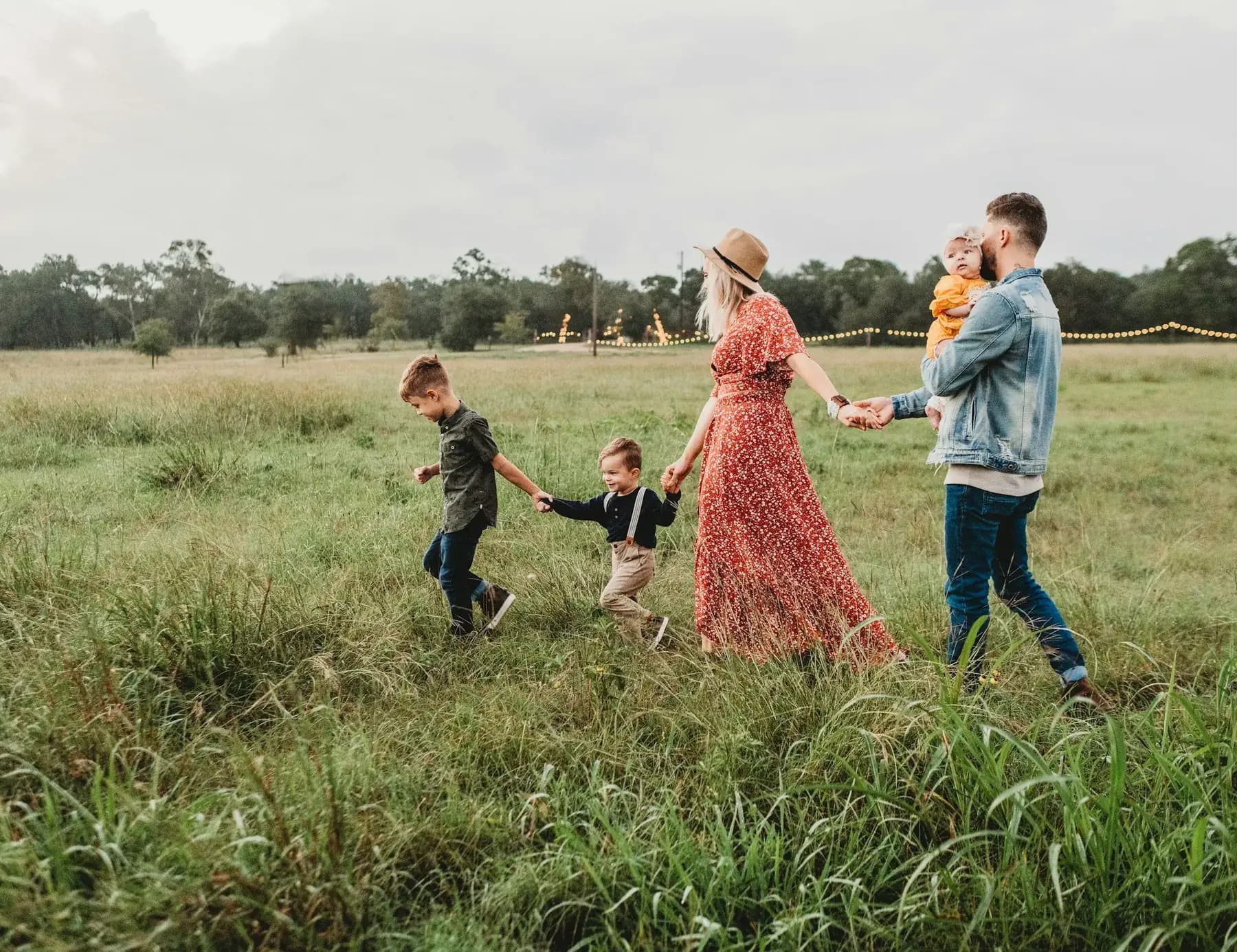 A mother and father walk hand in hand with their two young sons and baby daughter across a grassy field.
